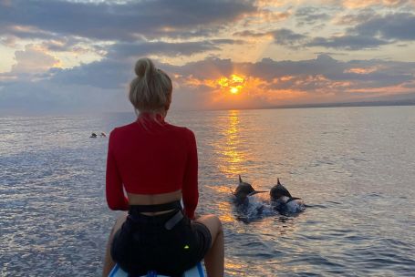 Woman on boat watching dolphins at sunset in Bali, Indonesia.