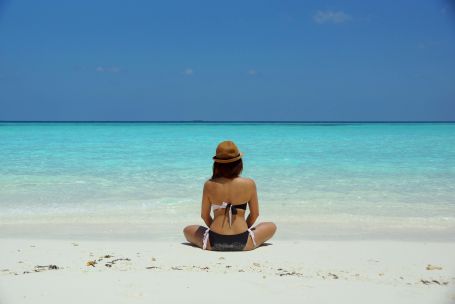 Rear view of a woman in a bikini and hat relaxing on a pristine beach in Maldives.